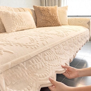 May include: Cream-coloured sofa with matching throw cushions. The sofa and cushions feature an embossed floral design. The sofa has a decorative skirt with a scalloped edge. The cushions are in shades of cream and tan.