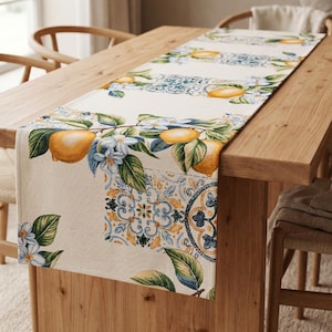 Pode incluir: Caminho de mesa retangular com um design de limões e flores. O caminho de mesa apresenta limões amarelos, flores azuis e folhas verdes sobre um fundo creme. O design inclui padrões de azulejos decorativos.