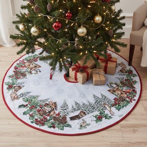 May include: A decorated Christmas tree with baubles and lights stands above a white tree skirt. The skirt has a red border and features a winter scene with houses, trees, and animals. Wrapped gifts with red bows are placed beneath the tree.