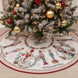 May include: A round Christmas tree skirt with a cream-colored background and a red border. The skirt features illustrations of nutcrackers, pinecones, and festive greenery. Gold and red ornaments adorn the Christmas tree.