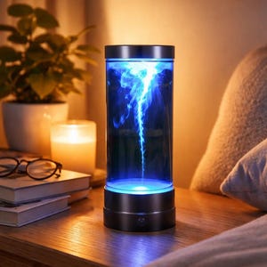 Könnte beinhalten: Eine zylindrische Lampe mit schwarzem Sockel und transparentem Körper, gefüllt mit wirbelnder blauer Flüssigkeit, die einen Plasmaeffekt erzeugt. Die Lampe steht auf einem Nachttisch aus Holz, mit einer Kerze, Büchern und einer Pflanze im Hintergrund. Die Lampe ist etwa 20 cm hoch.