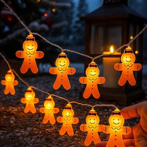 Op de afbeelding: Een lichtsnoer met verlichte peperkoekmannetjes. Elk oranje licht heeft een lachend gezicht, een vlinderdas en drie knopen. De lampjes zijn geregen aan een dunne draad, perfect voor feestdagen.