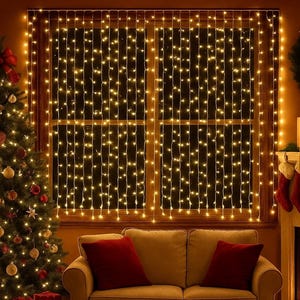 Op de afbeelding: Een gezellige woonkamer met een kerstboom, cadeaus en een bank. Het raam is versierd met lichtslingers, wat een feestelijke sfeer creëert. Rode kussens zorgen voor een kleuraccent op de neutrale bank.