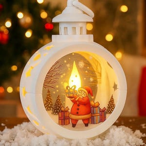 Puede incluir: Linterna navideña blanca con forma redonda y asa. La linterna presenta una figura de Papá Noel sosteniendo un regalo, rodeada de árboles de Navidad y regalos. La linterna tiene recortes en forma de estrella y una luz cálida.