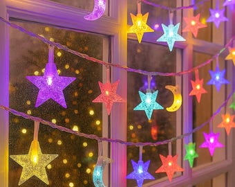 May include: A decorative string of fairy lights featuring star and crescent moon shapes. The lights are in a variety of colours, including yellow, purple, blue, and red. The lights are suspended in front of a window, creating a festive and decorative display.