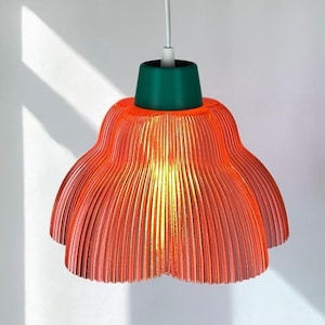 May include: A pendant light fixture featuring a translucent, ribbed, orange-red lampshade with a scalloped edge. The shade is attached to a solid dark green cylindrical top piece, which connects to a white electrical cord for ceiling suspension.