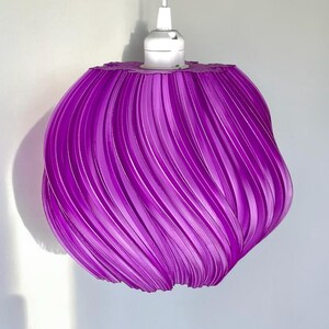 May include: A vibrant purple pendant light shade with a distinct spiralling, ribbed texture. The spherical shade features a glossy finish and is attached to a white electrical cord and a white socket fixture at the top centre of the structure.