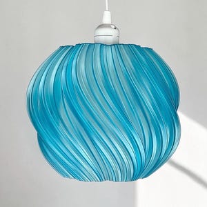 May include: A bright blue pendant light fixture featuring a spherical shade with a distinct vertical, swirling, ribbed texture. The lamp is suspended by a white cord attached to a white socket cap at the top of the translucent, textured blue shade.