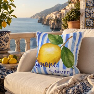 May include: A decorative square pillow with a watercolor lemon design. The pillow features a yellow lemon with green leaves and the words "Limone Summer" on a blue and white striped background. The pillow is on a beige chair.