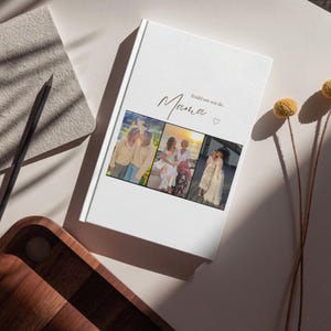 May include: A white photo album with the word "Mama" in script, and three photos. A pencil and notebook are next to the album, with a wooden tray in the corner. Dried flowers are on the right.