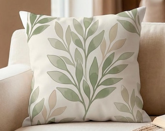 May include: A square throw pillow featuring a cream-colored background with a repeating botanical pattern of sage green and soft beige leaves. The design consists of stylized leafy branches arranged in a symmetrical, flowing layout across the fabric.