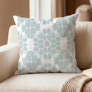 May include: A square throw pillow featuring a repeating geometric pattern of soft sage green rounded shapes on a crisp white background. The design consists of symmetrical, petal-like clusters arranged in a grid, creating a clean and balanced visual.