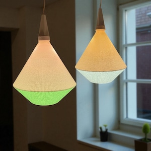 May include: Two pendant lights with a woven texture, cone-shaped shades. One light has a white top, transitioning to a green base. The other has a yellow top and a white base. The lights hang from white cords, creating a modern, decorative lighting fixture.