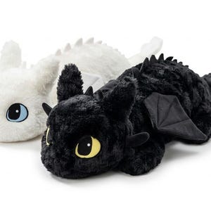 May include: Two plush dragon toys, one white and one black, are displayed side-by-side. The white dragon has blue eyes, while the black dragon has yellow eyes. Both have soft, textured fur, wings, and small horns.