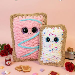 Pode incluir: Duas almofadas de pelúcia retangulares em forma de torrada, uma rosa com um redemoinho azul e a outra branca com granulado colorido. O texto "Toast Pattern" está acima das almofadas. Fatias de torrada, corações de doces e um pote de geleia são visíveis.