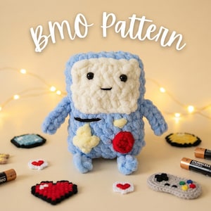 Puede incluir: Un personaje BMO azul y blanco tejido a ganchillo, con detalles amarillos y rojos. La imagen incluye accesorios de juego tejidos a ganchillo y pilas. El texto "BMO Pattern" está en la parte superior.