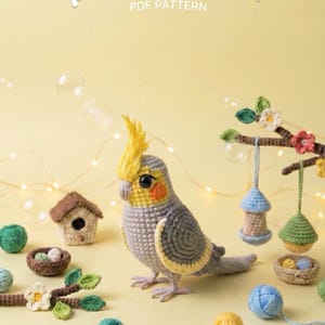 Könnte beinhalten: Ein gehäkelter Papagei mit gelbem Kamm und orangefarbenen Wangenflecken steht neben Miniatur-Häuschen und hängenden Dekorationen. Der Text "parrot pattern PDF pattern" ist ebenfalls enthalten.