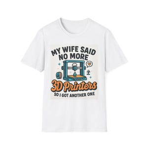 May include: White t-shirt featuring a colorful graphic with the text "MY WIFE SAID NO MORE 3D PRINTERS SO I GOT ANOTHER ONE." The graphic includes a 3D printer illustration and other design elements.