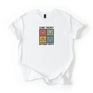 May include: White t-shirt featuring the text "SAME ENERGY DIFFERENT OUTFIT" and four square graphics. The graphics include a pizza slice, cowboy hat, hard hat, and party hat. The shirt is made of a soft material.
