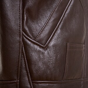 Puede incluir: Primer plano de una chaqueta de cuero marr&oacute;n con cintur&oacute;n y bolsillo. La chaqueta tiene una superficie texturizada y est&aacute; cosida con un patr&oacute;n decorativo.