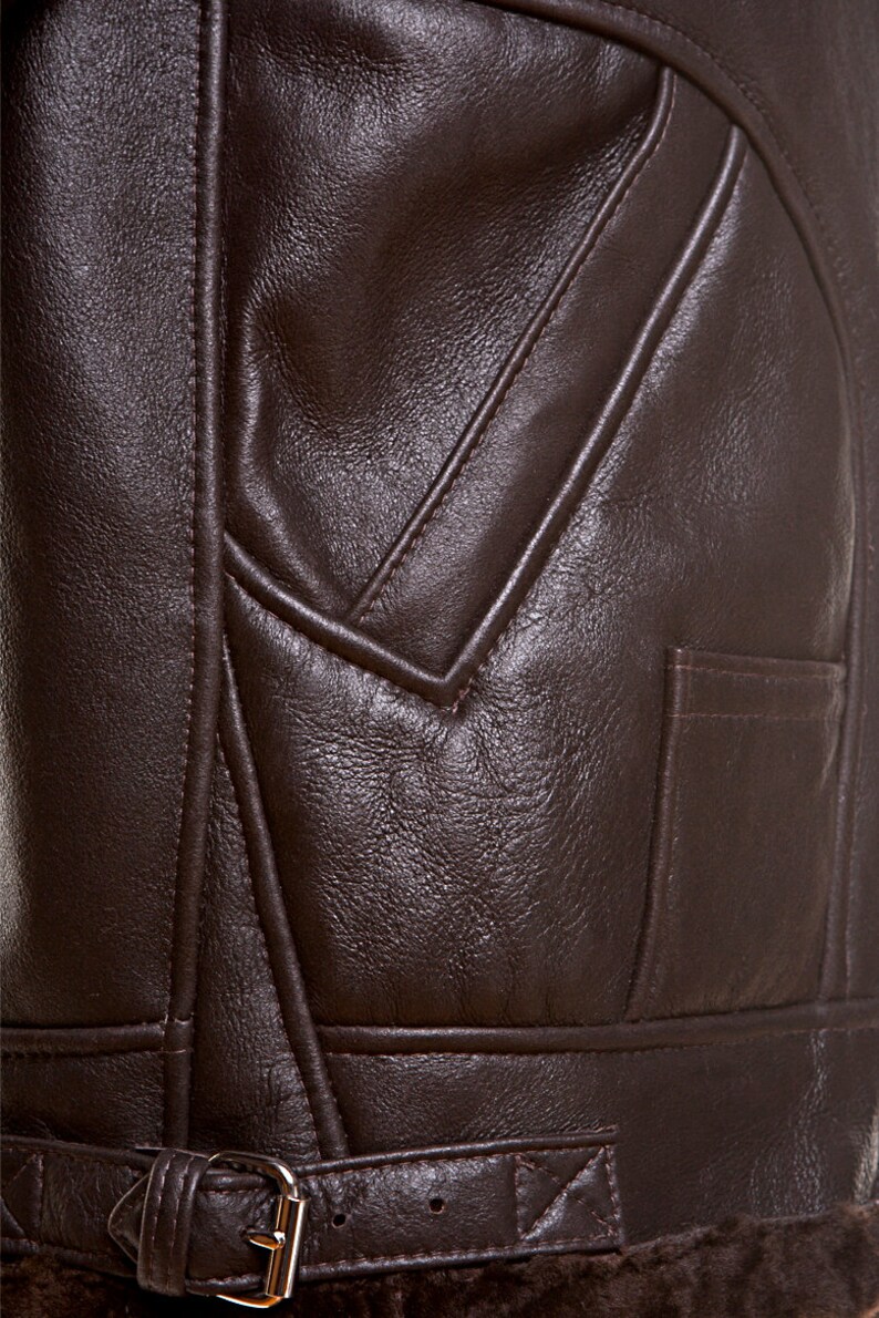 Puede incluir: Primer plano de una chaqueta de cuero marr&oacute;n con cintur&oacute;n y bolsillo. La chaqueta tiene una superficie texturizada y est&aacute; cosida con un patr&oacute;n decorativo.