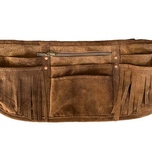May include: A brown leather tool belt with multiple pockets and fringe detailing. The belt has a zipper closure and copper rivets.