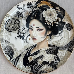 May include: Decorative porcelain plate featuring a portrait of a geisha. The plate has a gold rim and a black, white, and gray color scheme. The geisha is depicted with dark hair, red lips, and elaborate floral and cloud motifs.