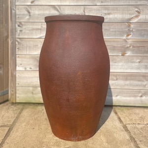 May include: A tall, cylindrical terracotta garden planter with a wide, flat rim and a slightly tapered base. The exterior surface features a textured, weathered finish in a deep, earthy reddish-brown tone, showcasing a consistent matte appearance.
