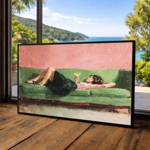 May include: A framed painting shows a person relaxing on a green sofa, holding a cocktail. The background features a pink wall and a coastal view of the sea and hills. The artwork is set against a wooden floor and a large window.