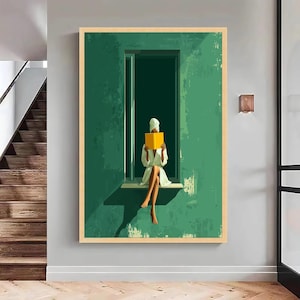 May include: A framed art print depicts a person in a white robe and towel, seated in a window, reading a yellow book. The artwork features a green wall and window frame, with a neutral-toned border.