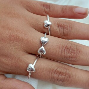 Peut inclure: Une main présente plusieurs bagues en argent, chacune ornée d'un cœur. Les bagues sont portées sur différents doigts, mettant en valeur les bijoux sur un fond neutre. Les bagues sont simples et élégantes.