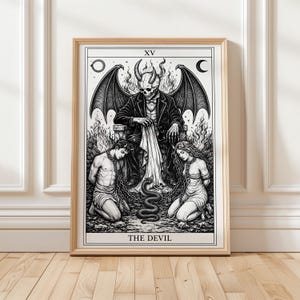Puede incluir: Impresión en blanco y negro enmarcada de una carta del tarot. Representa una figura de diablo esquelético con cuernos, alas y un traje. Dos figuras están encadenadas en la parte inferior, con una serpiente entre ellas. La carta está etiquetada como "THE DEVIL" y "XV".