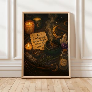 May include: A framed print depicting a mystical arrangement with candles, a smoking cauldron, and a bottle labelled "Moon Water." The text "I release all that no longer serves me" is visible. The artwork has a warm colour palette.