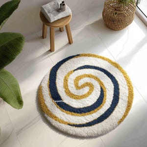 May include: A round, plush bath mat with a spiral design. The mat features a white background with a navy blue and golden yellow spiral pattern. The mat is on a white tile floor. A small wooden stool with a towel and toiletries sits nearby.