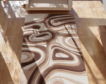 May include: A rectangular area rug with a layered, abstract design in shades of brown, beige, and cream. The rug features a swirling, organic pattern, with the text "CarpetPlazza" in the center. The rug is placed on a wooden floor.