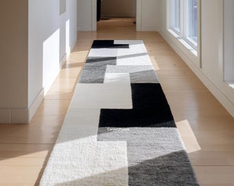 May include: A rectangular runner rug with a geometric pattern in black, white, and grey. The rug is placed in a hallway with hardwood flooring. The design features large, irregular blocks of colour, creating a modern aesthetic.