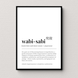 May include: A black framed print featuring the word "wabi-sabi" in a bold font, with Japanese characters above. The definition below describes the Japanese concept of finding beauty in imperfection. The frame is black.