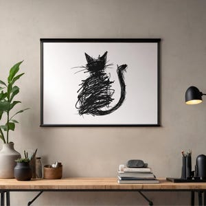 Puede incluir: Impresión artística abstracta en blanco y negro de un gato. El gato está representado en un estilo garabateado, con una cola larga y orejas puntiagudas. La obra de arte está enmarcada en un marco negro y se exhibe en una pared.