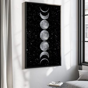 以下が含まれることがあります： 星が散りばめられた黒い背景に、月の満ち欠けを描いた額入りのアートプリント。 月の満ち欠けはグレーと白で表現され、黒いフレームが付いています。 アートワークは白い壁に飾られています。