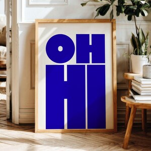 Peut inclure: Une affiche encadrée avec les mots "OH HI" en lettres bleues foncées. L'œuvre est présentée dans un cadre en bois clair, offrant un style moderne et minimaliste. Cette affiche est un ajout saisissant à la décoration intérieure.