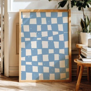 May include: A framed art print featuring a blue and off-white checkered pattern. The artwork is displayed in a natural wood frame. The print is rectangular and leans against a wall, suggesting a decorative piece for home decor.
