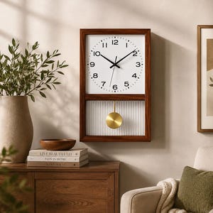 May include: A rectangular wall clock with a dark wood frame, a white face featuring black Arabic numerals, and black hands. Below the clock face is a glass panel with vertical fluting, showcasing a circular gold-toned pendulum.