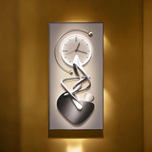 Puede incluir: Un reloj de pared moderno con marco rectangular. La esfera del reloj es blanca con manecillas negras y un acento circular dorado. Debajo, un diseño abstracto plateado con forma de corazón.