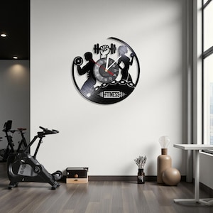 May include: Black vinyl record clock with a fitness theme. The clock features silhouettes of people working out, barbells, and the word "FITNESS". The clock hands are white and the numbers are visible.