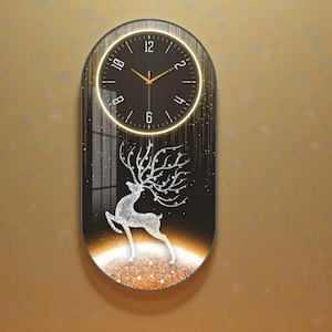 Può includere: Un orologio da parete ovale con quadrante nero e lancette dorate. L'orologio ha una luce circolare luminosa attorno al quadrante. Sotto, un'illustrazione di un cervo argentato su sfondo nero con base dorata glitterata.