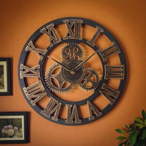 May include: A large, round wall clock with a black frame and bronze Roman numerals. The clock features decorative bronze gears in the center and bronze clock hands. The clock is mounted on an orange wall.