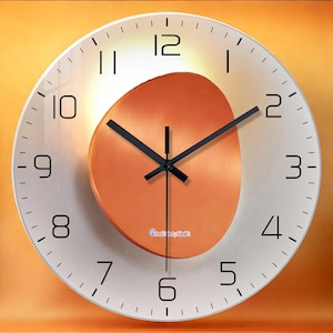 Può includere: Un orologio da parete rotondo con quadrante bianco e numeri neri. L'orologio presenta lancette nere e un design ovale arancione al centro. Il testo "Constant planet" è visibile sul quadrante.