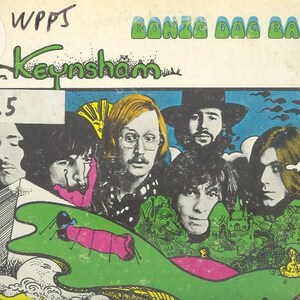 May include: Vintage album cover for the Bonzo Dog Band's "Keynsham." The artwork features a collage of faces, a green landscape with a pink insect, and the band's name in green bubble letters. A promotional copy sticker is visible.