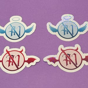 Puede incluir: Cuatro pegatinas con temática celestial. Dos pegatinas presentan alas de ángel y halos, mientras que las otras dos tienen cuernos y alas de diablo. Cada pegatina tiene un círculo con la letra "M" tachada.