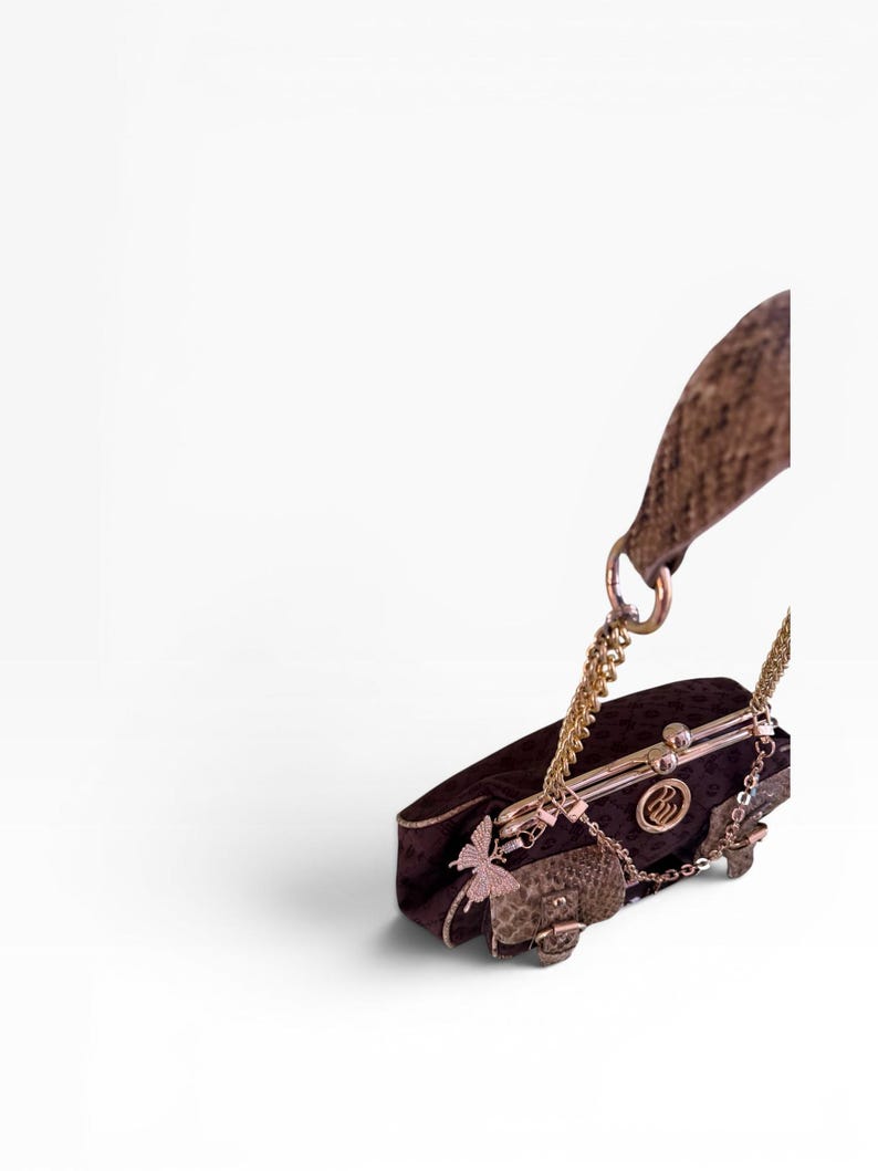 May include: A dark brown clutch bag with a gold chain strap and clasp. The bag features a butterfly charm and a small, patterned flap. The bag has a gold-coloured metal frame and a textured handle.